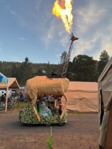 Art car shaped like a giraffe shooting flames from its head driving through the SOAK festival grounds
