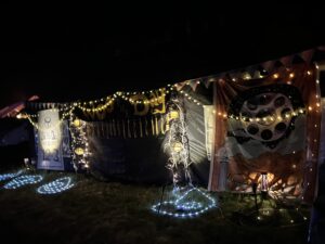 Win the Day theme camp decorated with string lights and movie reel artwork at night