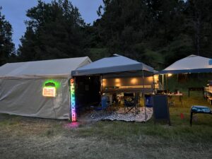 Pickleodeon theme camp at dusk with glowing marquee sign, vertical LED Pickleodeon sign, and warm string lights under canopy