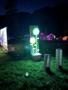 Illuminated white flower sculpture on green trellis glowing at night with festival backdrop