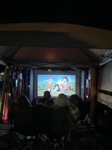 Audience watching animated film Kiki's Delivery Service on projection screen inside the Pickleodeon outdoor theater tent
