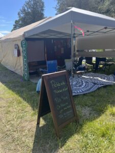 Pickleodeon camp during daytime with vertical green sign, chalkboard menu advertising Pickle-ade, and lounge area
