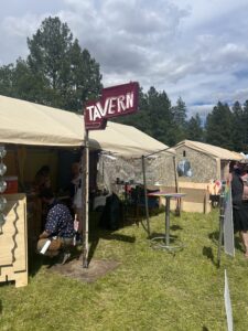 Theme camp with vintage Tavern arrow sign, camo netting decoration, and festival goers relaxing