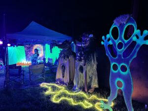 Eerie nighttime art installation featuring illuminated ghost sculpture and mysterious robed figures under black light