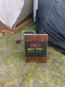 Wooden A-frame chalkboard sign advertising D&D Party Style event on Sunday 1-3pm at festival camp