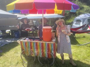 Pickleodeon crew serving happy festival visitor at the rainbow-fringed pickle cart, crew member in witch costume, visitor with pickle and drink
