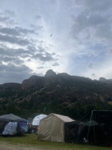 Dramatic view of Wolf Creek canyon with rocky cliffs, moody clouds, soaring bird, and colorful festival tents below