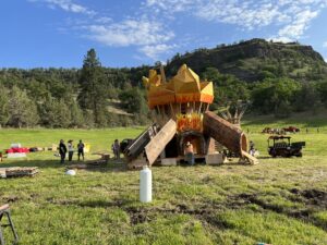 Large wooden art installation shaped like a campfire with yellow flame structures being constructed in an open field