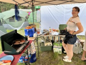 Camp member cooking burgers and sausages on a camp stove under a canopy at the theme camp