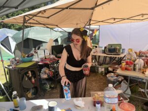 Festival attendee in black outfit with sunflower hair accessories preparing drinks at theme camp kitchen