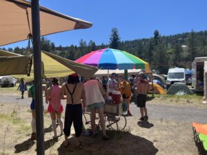 Festival goers gathering around the Pickleodeon rainbow umbrella cart to get pickle drinks