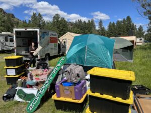 Pickleodeon camp unloading gear from U-Haul truck with storage bins and LED sign visible among tents