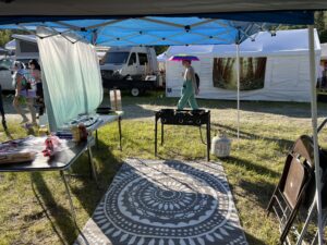 Theme camp kitchen setup with camp stove under blue canopy as festival goer walks by with rainbow umbrella