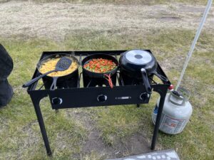 Three-burner camp stove cooking scrambled eggs and sautéed peppers at theme camp