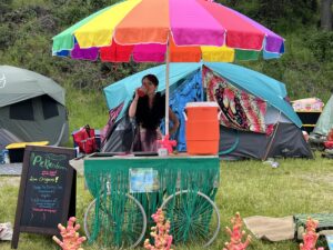 Pickleodeon pickle cart decorated with green grass fringe and coral props under rainbow umbrella with crew member serving