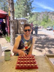Smiling festival goer in galaxy cat tank top playing Guess Who at the camp game area