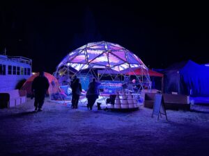 Illuminated geodesic dome called Hypnodrome with LED panels creating colorful light patterns while people gather inside